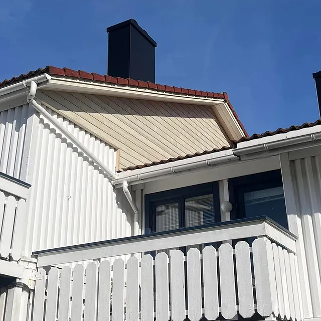 Nærbilde av balkonger på et hvitt rekkehus med røde tak og mørke vinduskarmer.